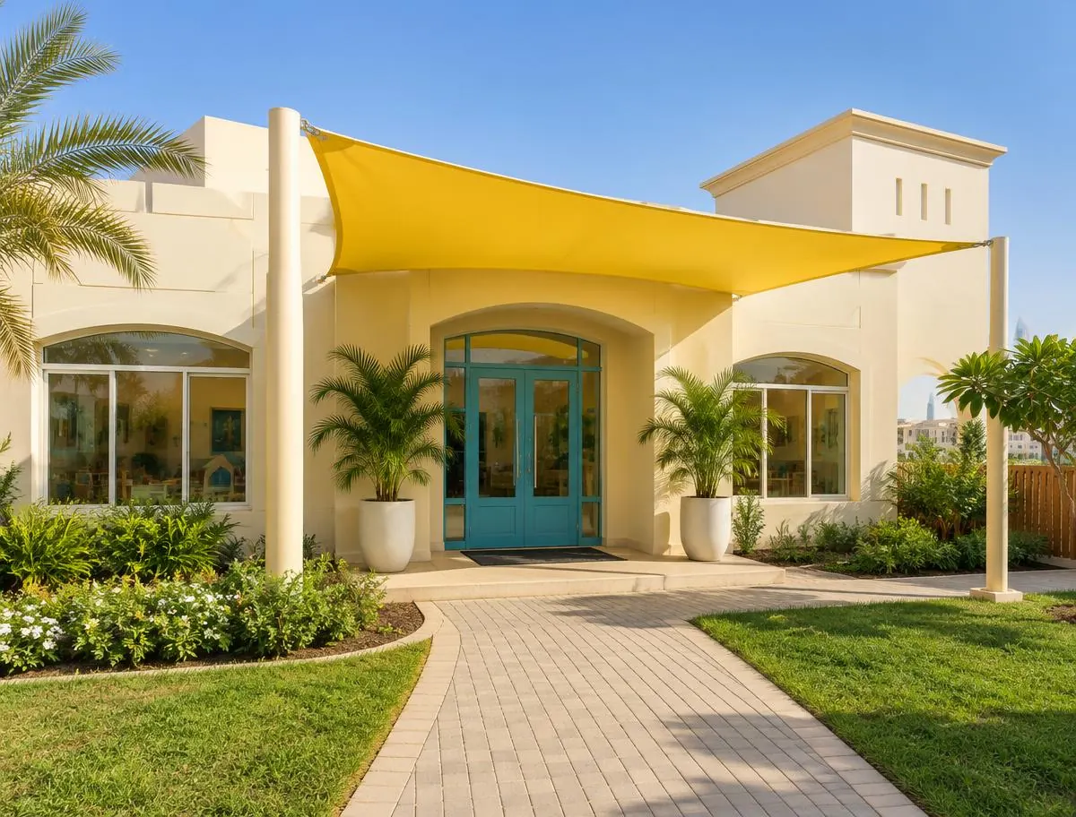 Cream nursery building with a teal front door, a yellow shade canopy and palm planters